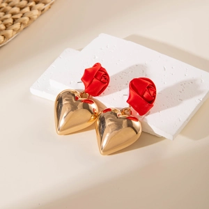 Close-up of red fabric rose and glossy gold heart earrings on a stone surface