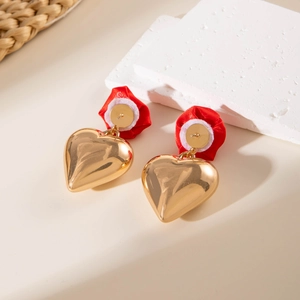 Detail of red ribbon bow and polished golden heart dangle earrings on a textured background