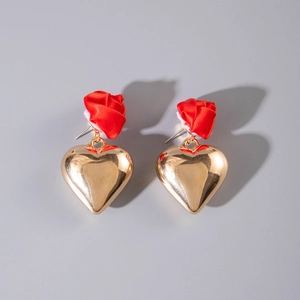 Detail of gold heart earrings with red satin rose accents on a neutral gray background