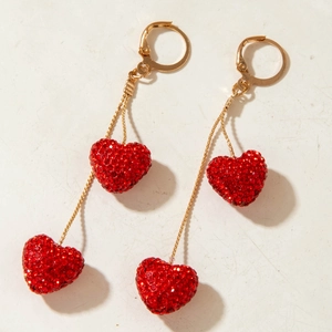 Detail of red rhinestone heart earrings with golden leverback dangling on a beige surface