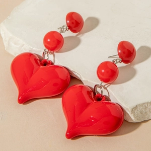 Detail of red heart drop earrings with glossy finish on a textured stone surface