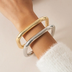 Polished gold and silver square bangles styled on a model's wrist with a white sweater