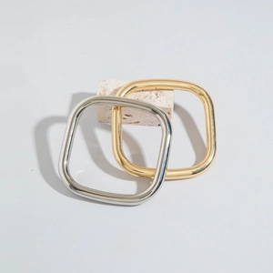 Close-up of thick square metal bangles in gold and silver finish on stone base