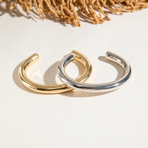 Close-up of minimalist gold and silver C-shaped tube bracelets with high-polish mirror finish