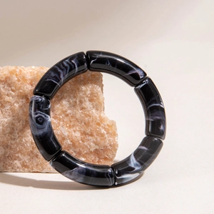 Detail of a black and white ink marble texture acrylic cylinder bracelet on a natural stone