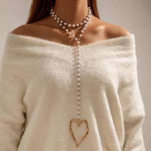 Détail macro d'un collier de perles en Y avec un pendentif cœur doré texturé