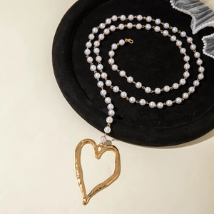 Détail d'un long collier de perles avec un grand pendentif cœur en or martelé sur velours noir