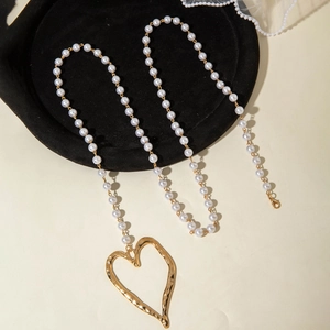 Détail d'un grand pendentif cœur doré martelé sur un collier de perles multicouche