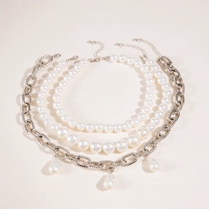 Ensemble de trois colliers superposés avec perles et pendentifs sur un fond beige neutre