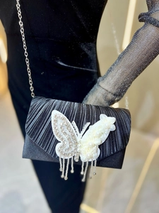 Détail d'une pochette de soirée plissée noire avec papillon strass et fleurs en perles