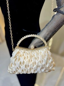 Detail of champagne satin clutch with pleated texture and rhinestone metal handle