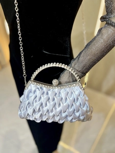 Detail of silver satin clutch with pleated layers and sparkling rhinestone handle
