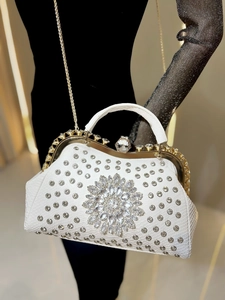 Close-up of luxury white evening bag with crystal flower decoration and gold chain strap