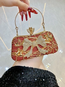 Détail d'une pochette rouge à paillettes avec notes de musique dorées et nœud en strass