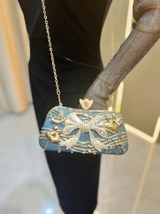Détail du sac de soirée à paillettes bleues avec notes de musique d'or et nœud strass