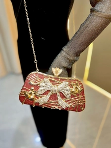 Détail de la pochette de soirée rouge pailletée avec notes dorées et nœud en cristal