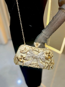 Détail de pochette dorée avec nœud en cristal et motif musical sur une robe noire