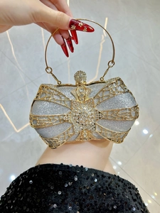 Close-up of luxury silver evening clutch featuring golden bow frame and sparkling crystals