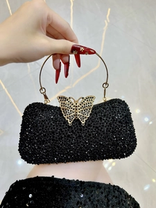 Detalle de bolso de fiesta con pedrería negra, cierre de mariposa dorado y asa de anillo