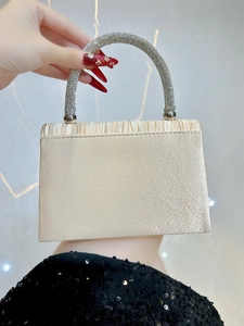 Detail of champagne gold satin evening bag featuring a pleated design and crystal handle