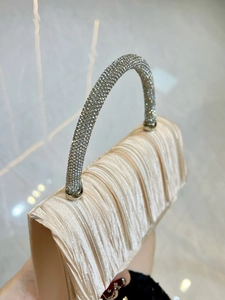 Close-up of champagne silk evening bag with pleated fabric and rhinestone handle