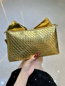 Detailed view of a gold woven evening clutch featuring a large decorative bow ornament