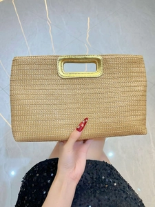 Close-up of natural straw clutch bag featuring a polished gold metal handle and woven texture