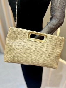 Detail of beige woven straw clutch featuring hollow gold metal handles and chain strap