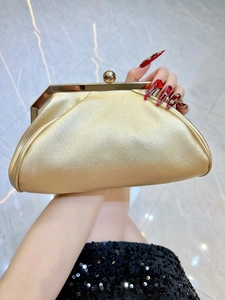 Détail de la pochette de soirée dorée avec fermoir sphérique tenue par un mannequin