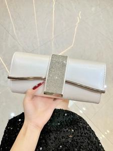 Close-up of white clutch featuring cross pattern and rhinestone band with golden clasp
