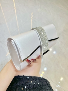 Detailed close-up of white evening clutch bag featuring sparkling rhinestone strap and metallic trim