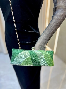 Détail d'une pochette de soirée à strass verts avec chaîne dorée sur velours noir