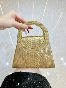 Macro shot of gold snakeskin textured handbag with large circular handle and trapezoid shape