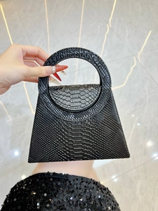 Detail of black faux snake skin texture on a luxury trapezoid handbag with ring handle