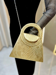 Detailed close-up of a gold snake-embossed handbag with round handle and silver chain strap