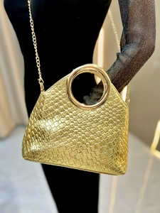 Detail of gold woven handbag with metal ring handle and crossbody chain strap