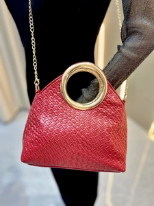 Detail of red woven handbag featuring a metallic gold circular handle and chain strap