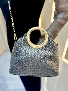 Close-up of black woven texture handbag featuring a wide gold circular metal handle