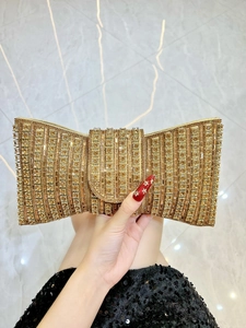 Close-up of sparkling gold bow-shaped clutch bag with rhinestones held by a model