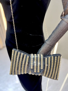 Detail of elegant black velvet bow clutch with gold rhinestones and metallic chain