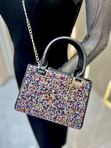 Close-up of sparkling colorful rhinestones on a black evening bag with a gold chain strap