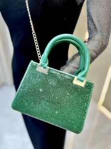 Detail of green rhinestone evening bag with gold chain strap on black outfit