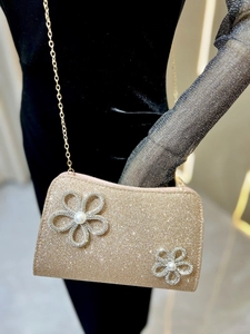 Detail of gold glitter evening clutch bag featuring rhinestone flowers and a pearl center