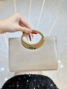 Detail of a sparkling gold evening clutch bag with round metal handle held by a hand