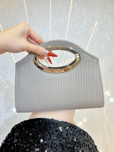 Close-up of woven gray clutch bag featuring a distinctive silver metal ring handle