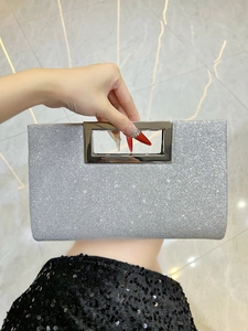 Detail of silver glitter evening clutch bag with metal handle held against a sequin dress