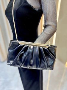 Detail view of black pleated evening clutch with elegant gold frame and chain strap