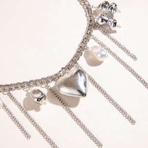 Dettaglio della collana con nappine argentate, cuore, perle barocche e charms geometrici
