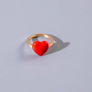 Detailansicht eines Goldrings mit einem leuchtend roten Harzherz auf glattem Band