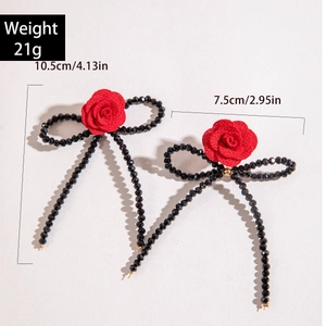 Détail de boucles d'oreilles nœud rose rouge avec perles noires et longues franges et tailles